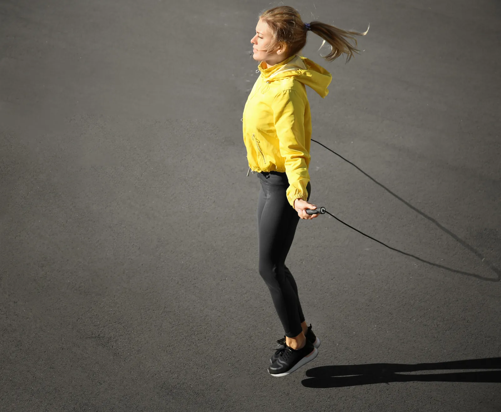 An active woman in a sunshine-yellow jacket jumping rope
